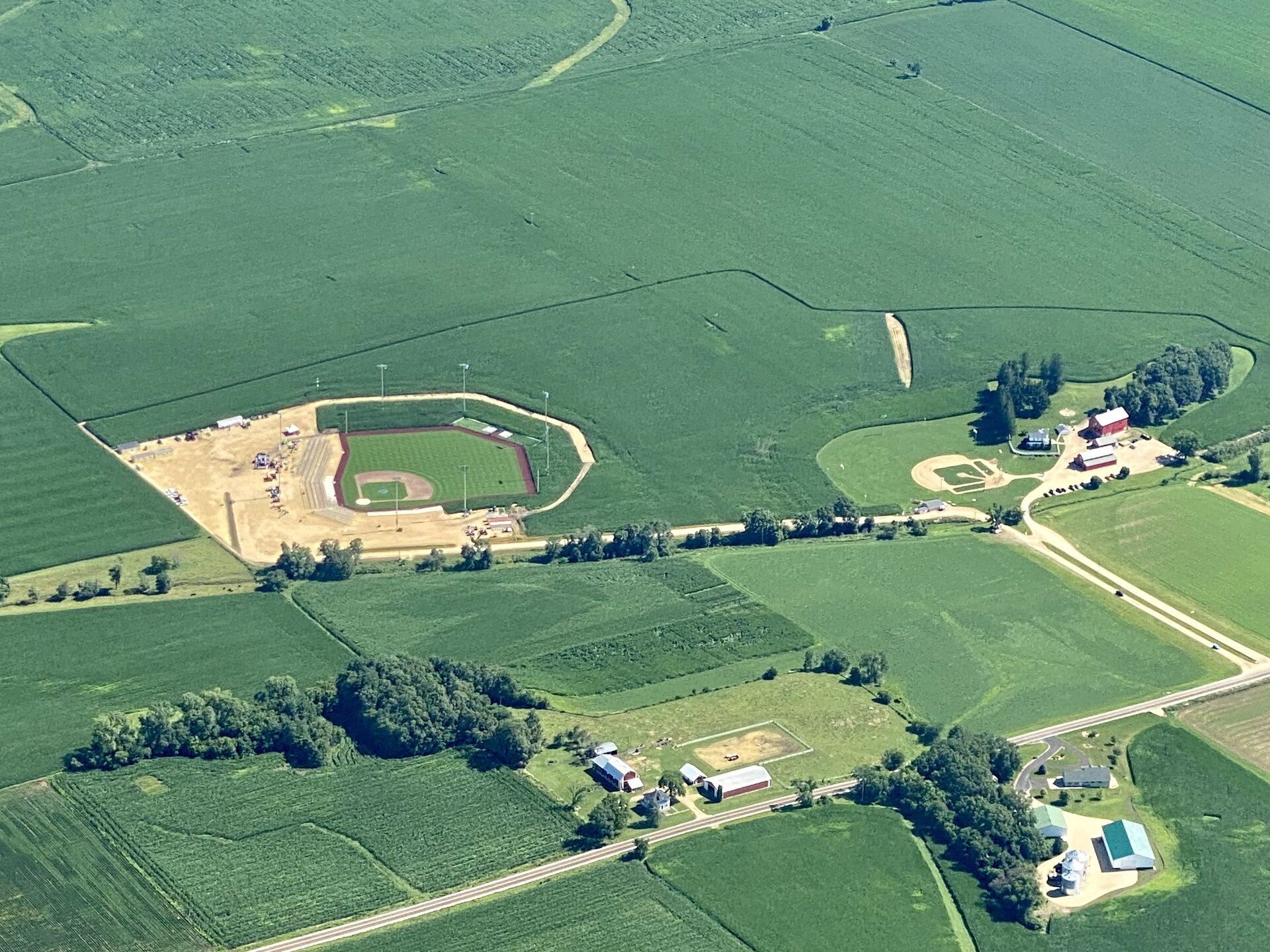 Aerial view of the Field of Dreams movie site and the MLB ballpark in Dyersville, Iowa — two baseball fields carved out of surrounding cornfields, with the farmhouse and red barn nearby